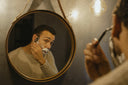 A man shaving in a round mirror.