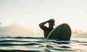 a guy sitting on his surfboard in the ocean at golden hour