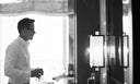 A black and white photo of a man looking at himself in the mirror. He's thinking, "Am I wearing too much cologne?"