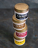 A stack of 4 cans of Layrite, each a different product.