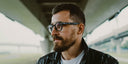 A man under an overpass with a beard and glasses.