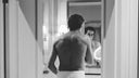 Man in towel looking at bathroom mirror during morning grooming routine, black and white photo illustrating self-assessment and preparation