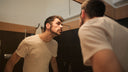 A man leans toward a bathroom mirror studying his own face, illustrating end of summer sun damage and dark spots.
