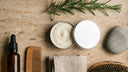 Flat-lay from above of a small tin of whipped tallow on a warm-toned bathroom counter.