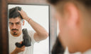 Guy blow drying his hair in the mirror