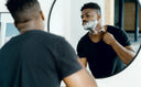 Man applying shaving cream and shaving with a razor in a round mirror