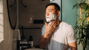 A man looking in the mirror applying shave cream.