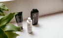 Three body washes on a counter with a bit of plant in the left corner.