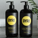 Two black bottles of BYRD shampoo and conditioner on a gray surface with a blurred background.