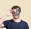 Man with a black face mask holding a product container against a beige background
