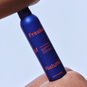 Blue sunscreen spray bottle labeled 'Freaks of Nature' held against a light blue background.