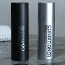 Black shampoo bottle and silver conditioner bottle on a marble surface with a blurred background.