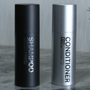 Black shampoo bottle and silver conditioner bottle on a gray surface with a neutral background