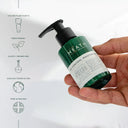 Hand holding a green bottle labeled 'Heath' with sustainability features on a white background