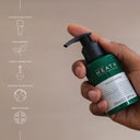 Hand holding a green Heath moisturizer bottle with brand information on a beige background
