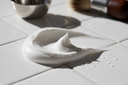 A premium men’s grooming editorial image featuring a soothing shave cream texture on a clean white surface, soft natural shadows, subtle hydration droplets, minimalist styling, close-up macro beauty photography, high contrast, ultra sharp detail, modern men’s skincare aesthetic, photographed like Aesop or Le Labo campaign, 4K, photorealistic