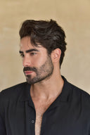 Man with styled hair and beard wearing a black shirt against a beige background