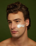 Man with a small amount of cream on his face against a green background