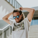 Man wearing sunglasses and a white t-shirt with a graphic design, standing outdoors.