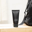 Black tube of CARDON SPF + Moisturizer  on a wooden surface with a black backpack in the background.