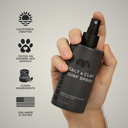 Hand holding a black spray bottle labeled 'Salt & Clay Surf Spray' with certification icons on a gray background.