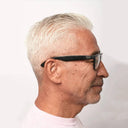 Side profile of a person with short gray hair wearing black glasses against a white background