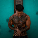 Person with tattoos standing under a shower against a teal wall