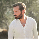 Man in a white shirt standing in an outdoor setting with trees in the background