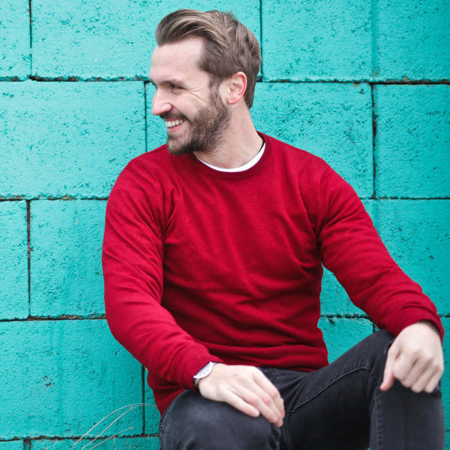 Man in a red sweater sitting against a teal brick wall