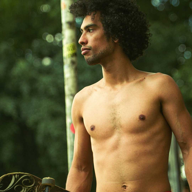 Man with a muscular build standing outdoors with a blurred natural background