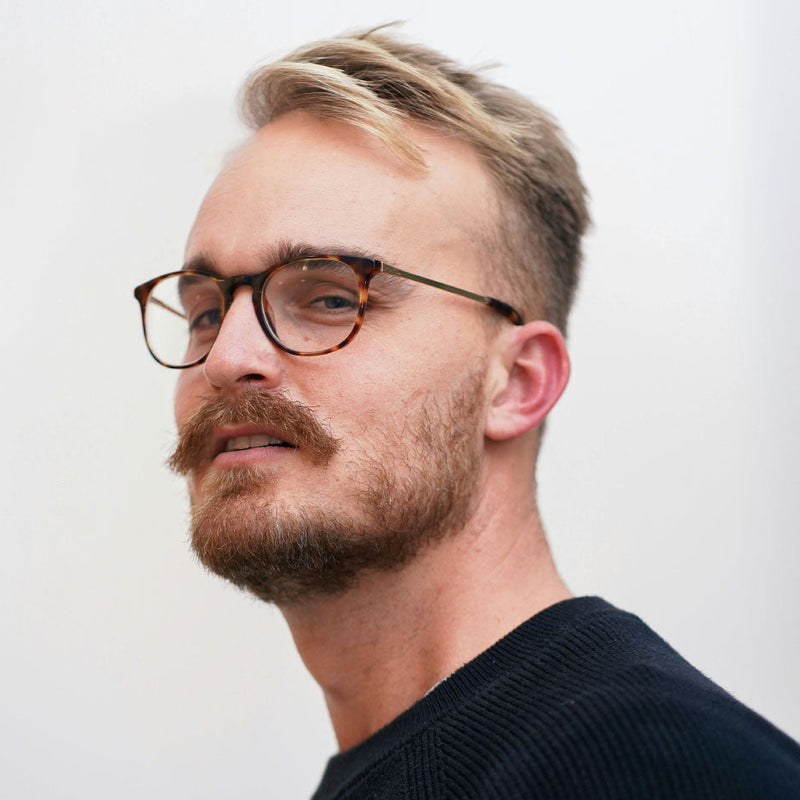 Man with glasses and a beard against a plain background