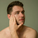 Man with a beard touching his face against a plain background